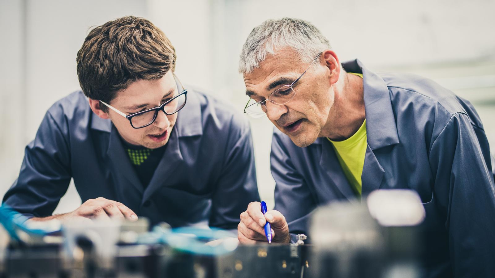 a older-generation man passing down his construction knowledge to a younger-generation man