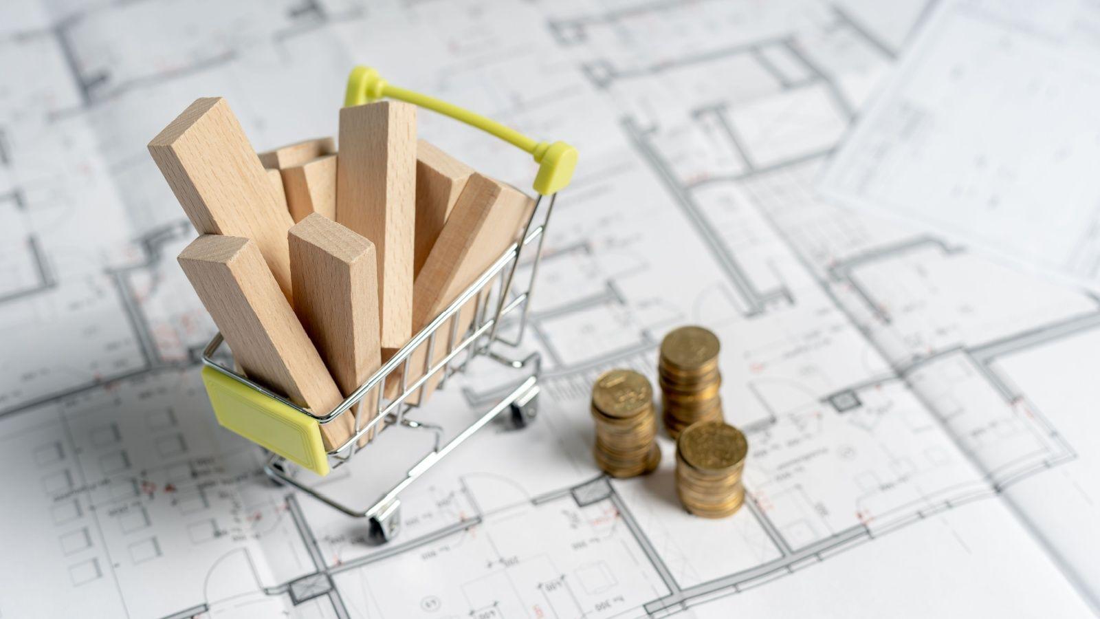 wooden blocks in a shopping cart on top of construction blueprints next to gold coins