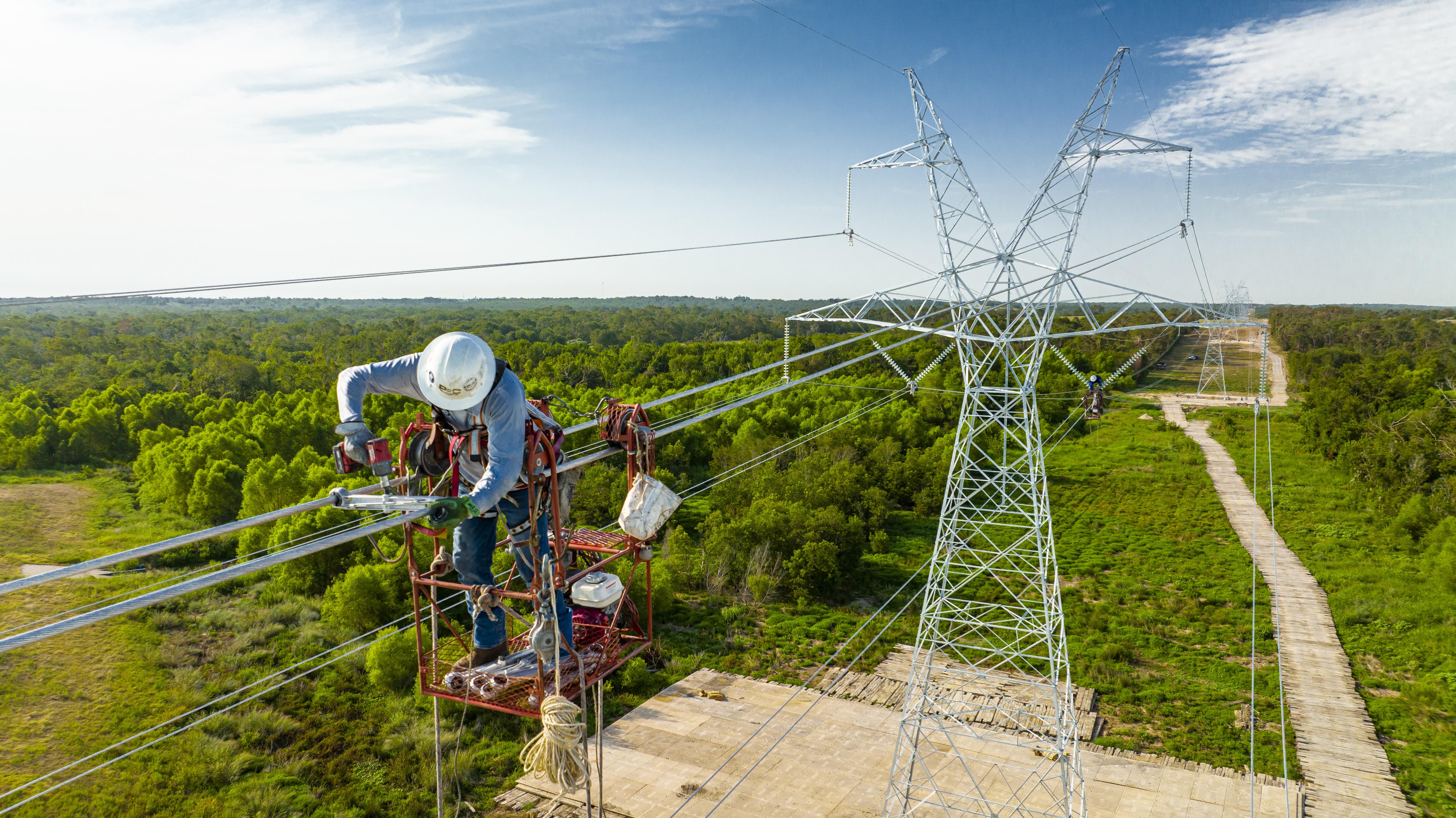 A line worker rides a motorized cart 125 feet in the air to attach spacer-dampers along newly installed transmission towers outside of Fairfield, Texas.