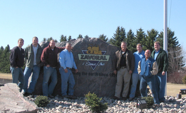R.J. Zavoral and Sons employees taking a photo next to a big rock with R.J. Zavoral company logo painted on it.
