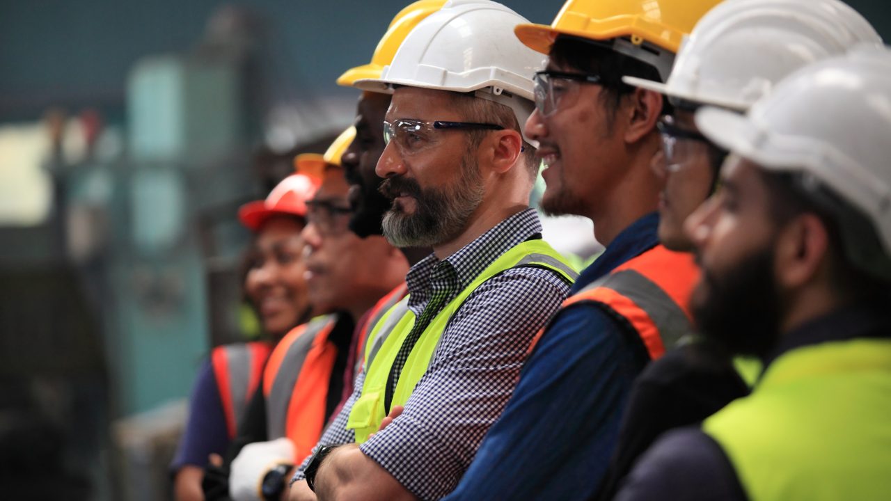 Construction workers with safety vests and safety hats standing in a line taking a group photo.