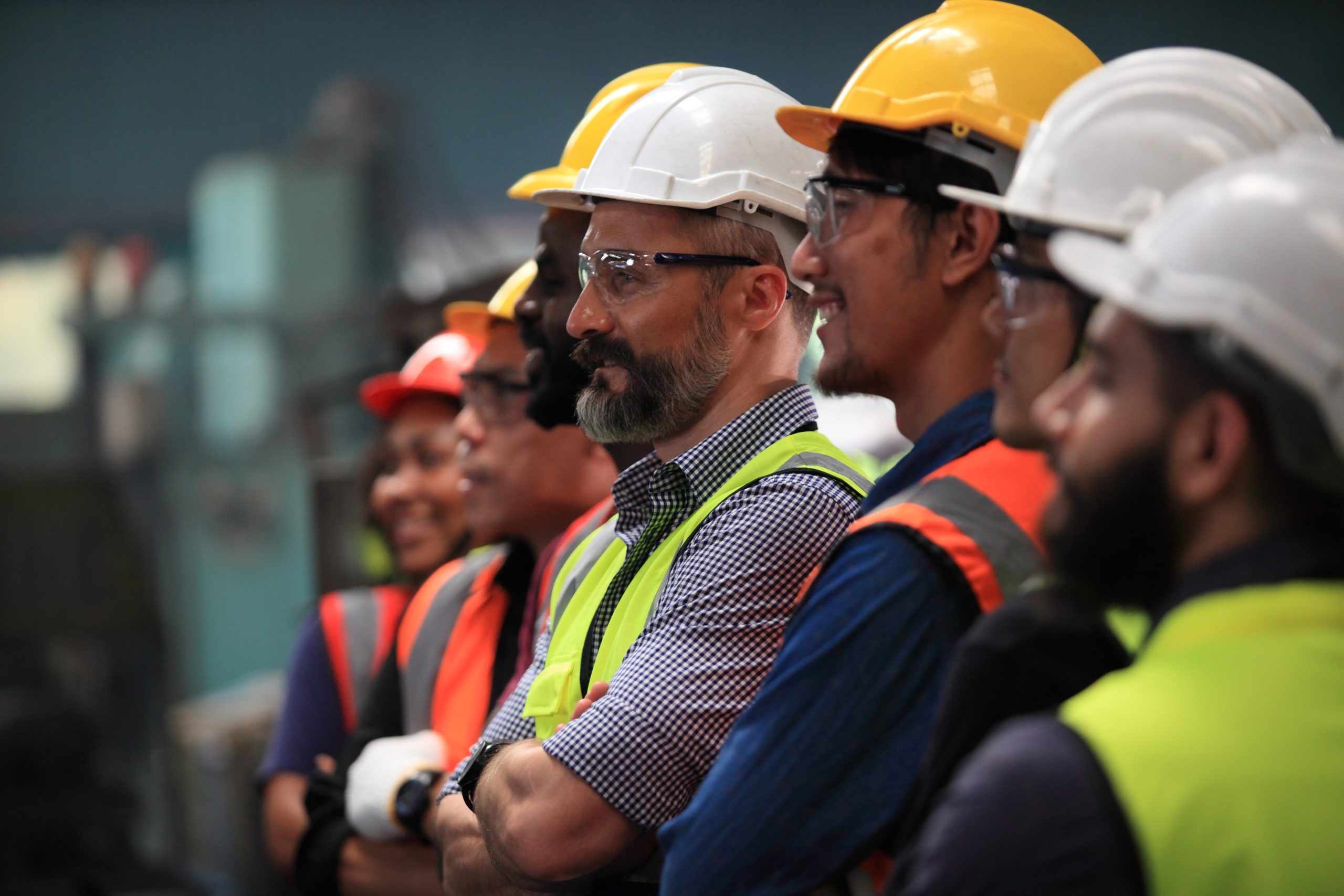 Construction workers with safety vests and safety hats standing in a line taking a group photo.