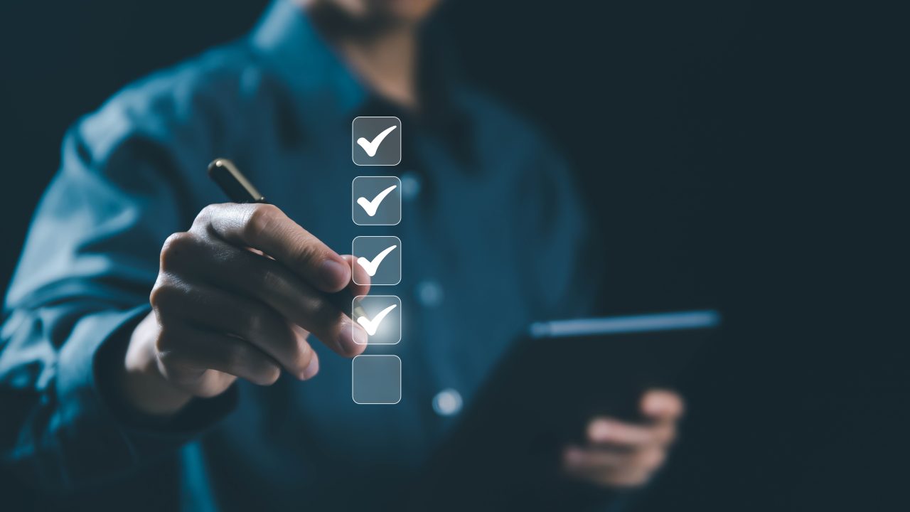 A man in a blue shirt holding a tablet and checking off task boxes with a pen.
