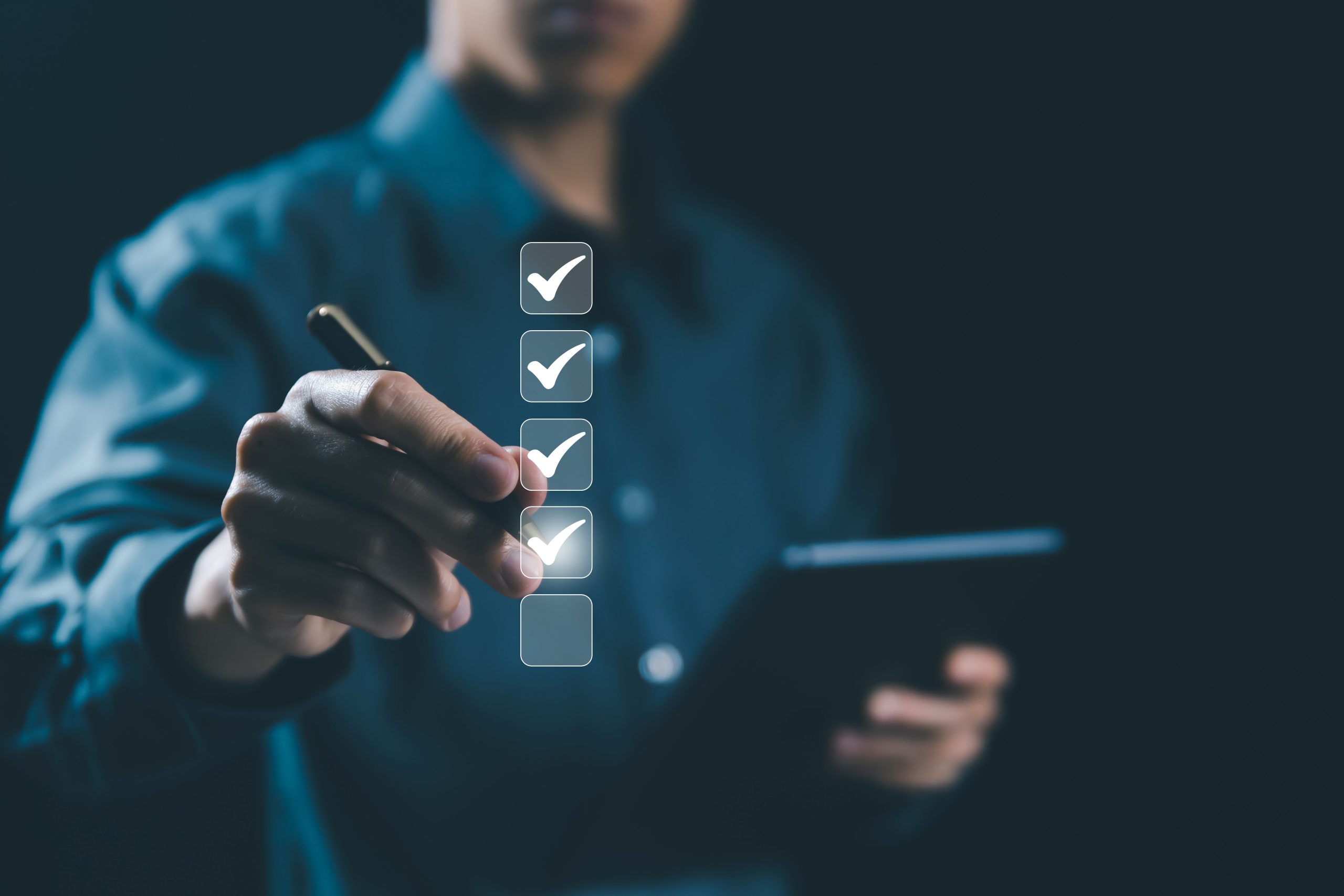 A man in a blue shirt holding a tablet and checking off task boxes with a pen.