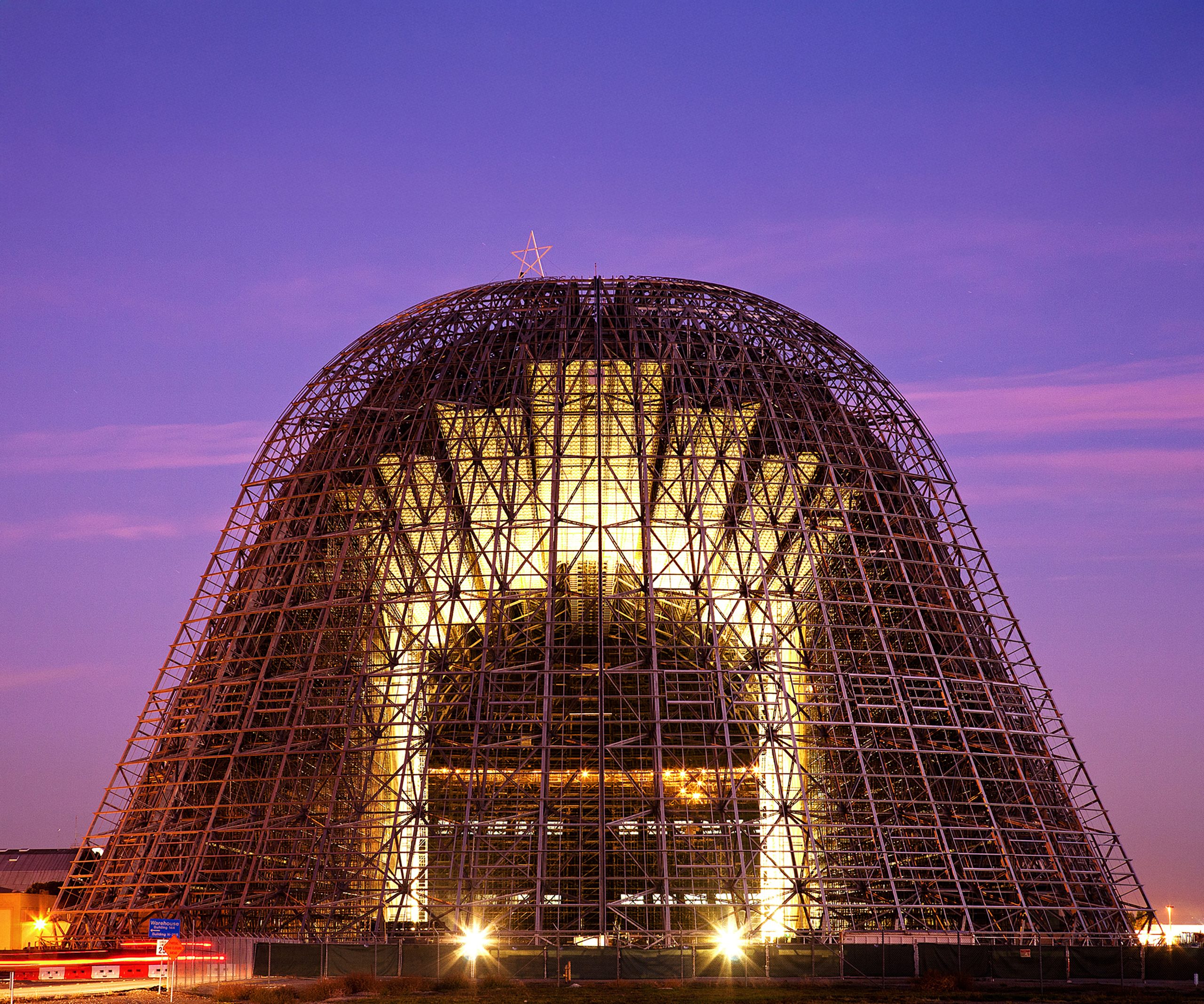 01_hangar1illuminated Hangar One at NASA's Ames Research Center illuminated at dusk, showcasing its massive steel lattice frame structure topped with a star against a purple twilight sky.