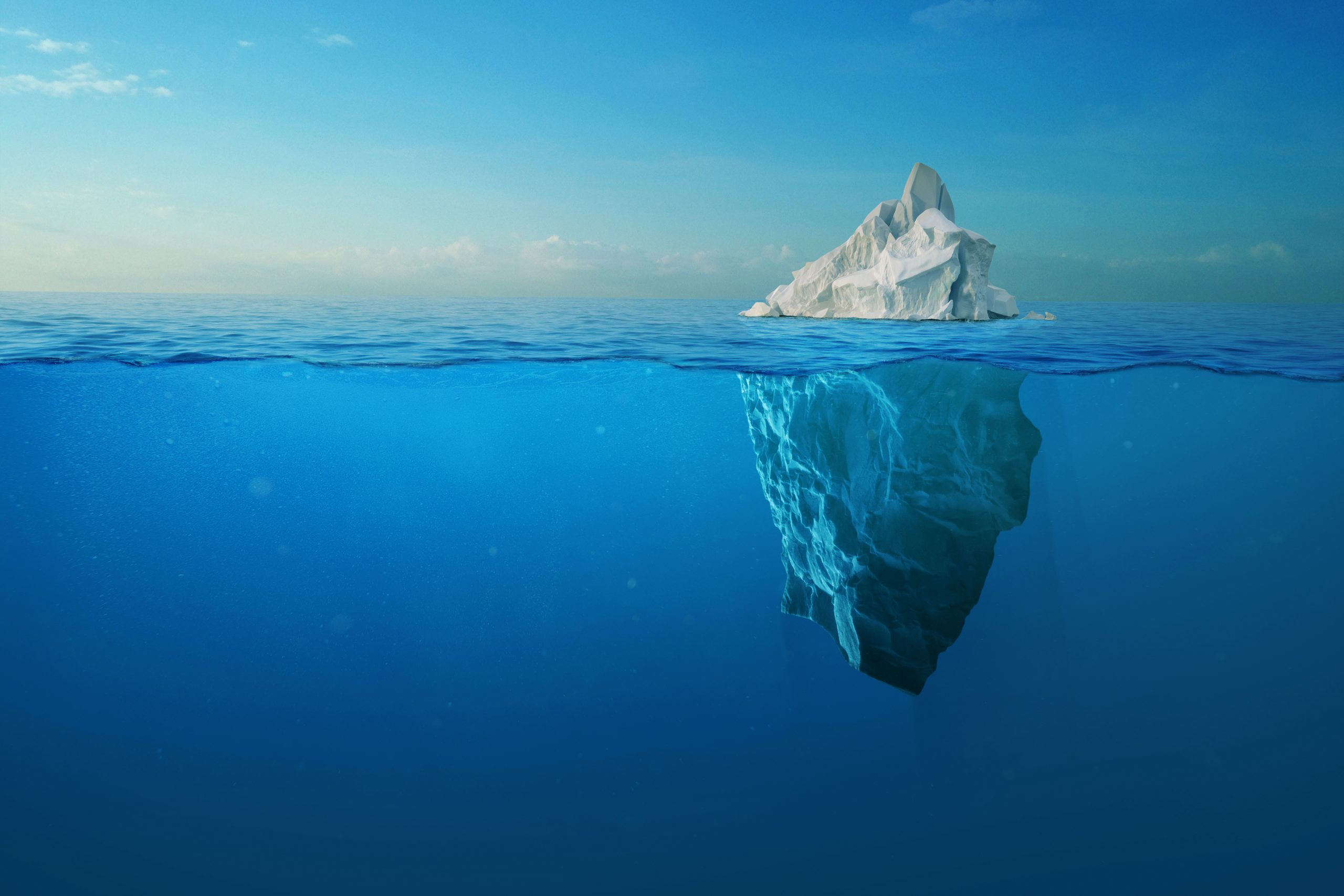 An iceberg floating in open ocean, showing both its small visible peak above the waterline and its much larger mass submerged below the surface.