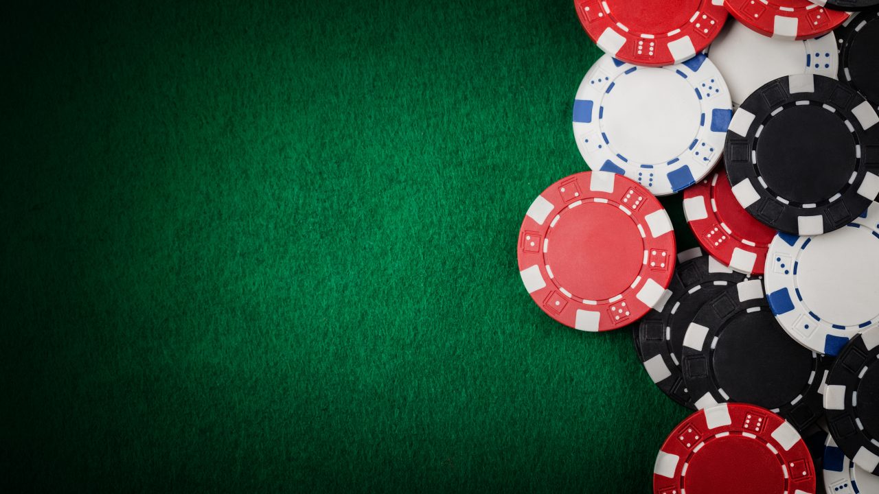 Red, white, black and blue poker chips scattered on a green felt casino table surface.