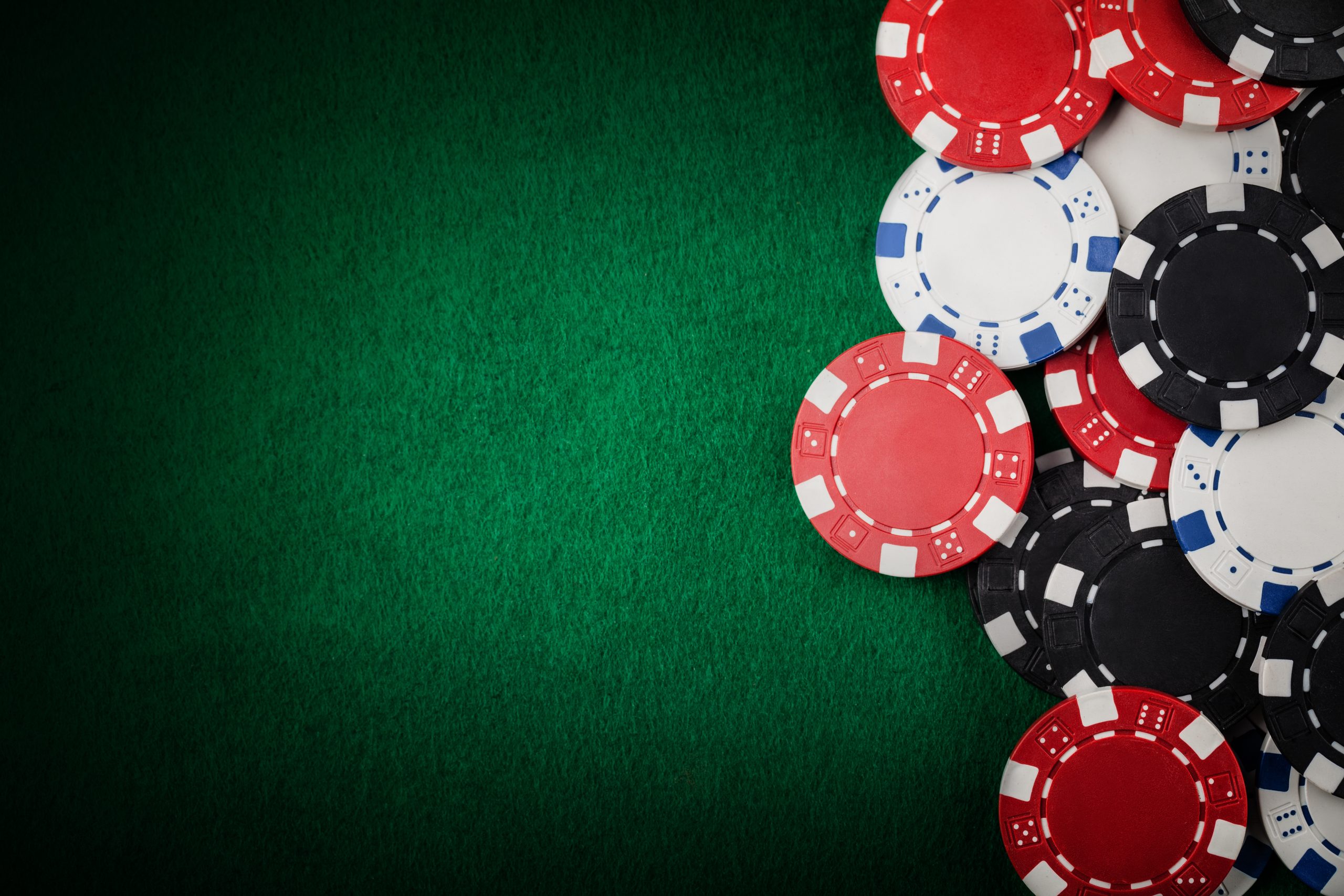 Red, white, black and blue poker chips scattered on a green felt casino table surface.