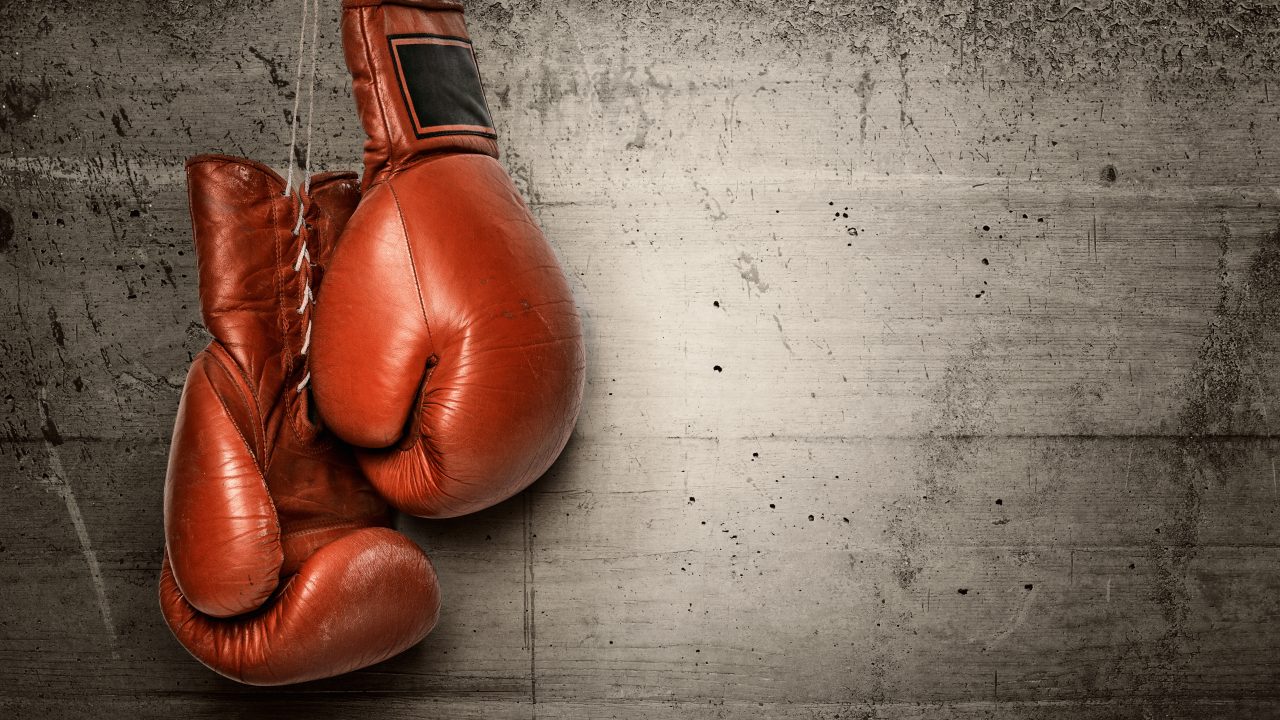 A pair of worn red leather boxing gloves hanging against a weathered concrete wall.
