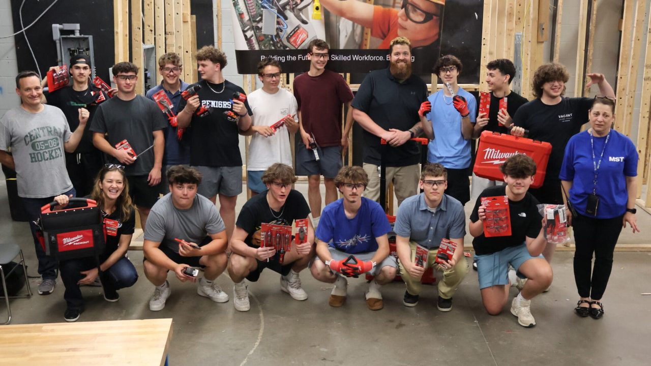 Students and instructors at Manchester School of Technology posing with Milwaukee Tool equipment in a vocational classroom, in front of a Bring Back the Trades banner reading "Building the Future Skilled Workforce."