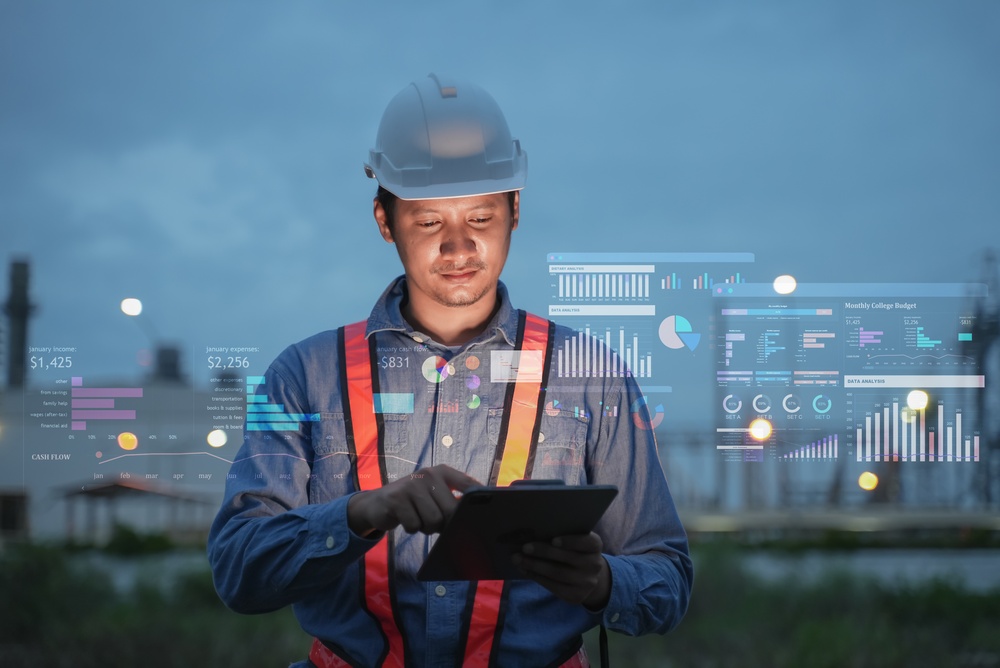 A construction worker in a hard hat and safety vest reviewing a tablet, surrounded by floating digital data dashboards and analytics displays on a jobsite at dusk.