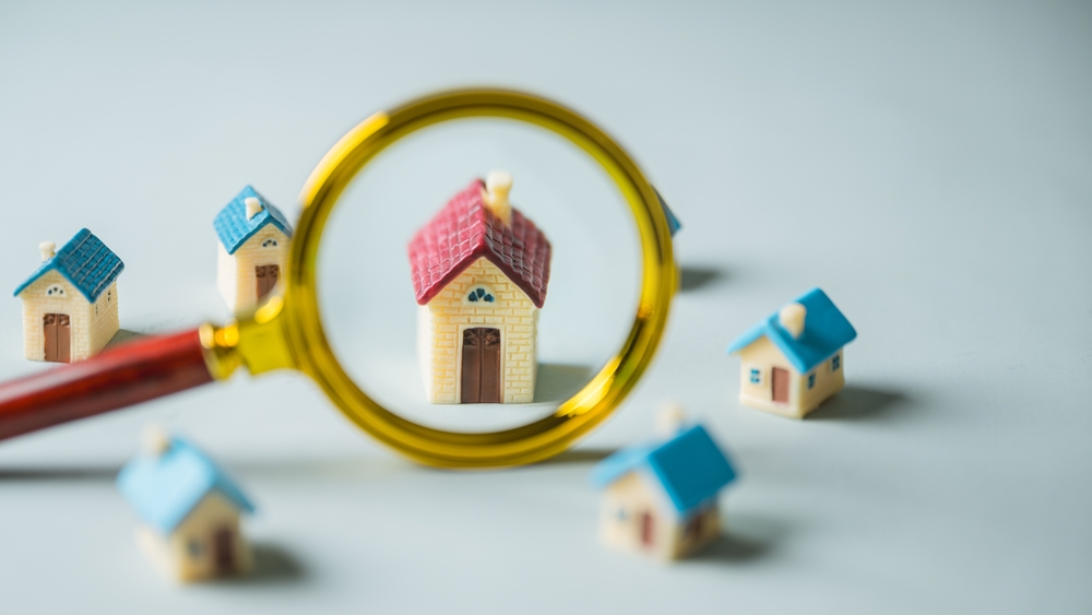 Miniature toy houses with a magnifying glass highlighting one home, symbolizing the search for real estate or housing amid economic uncertainty