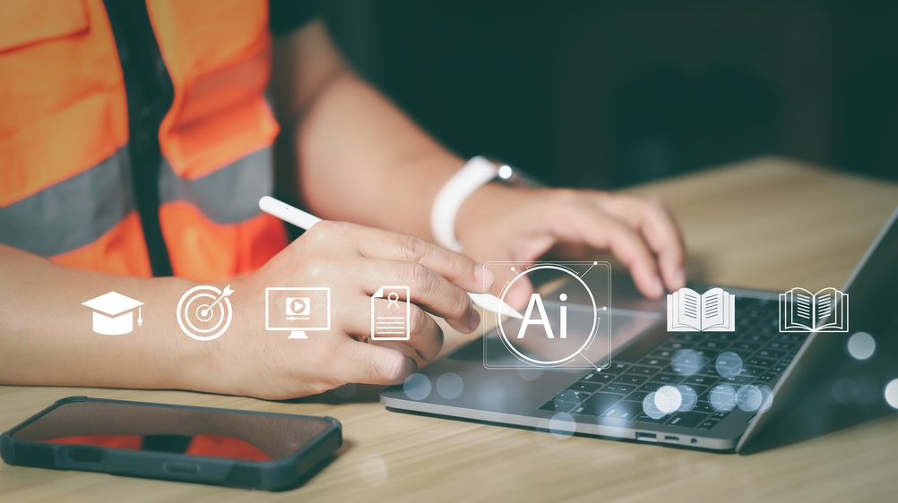 A construction worker in a high-visibility vest using a laptop and stylus, with AI, education and document icons overlaid representing digital learning and AI tools in construction.