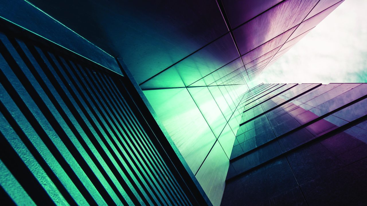 An abstract, upward-angle view of a modern high-rise facade with teal and magenta-toned glass and metal panels converging toward a bright, cloudy sky.”