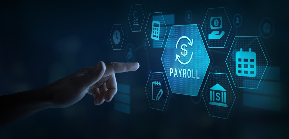 A hand reaches toward a glowing digital interface of hexagonal icons centered on a ‘Payroll’ button with a dollar sign and circular arrows, surrounded by icons for a calculator, document, clock, calendar, notepad, bank and cash in a hand, against a dark blue background.